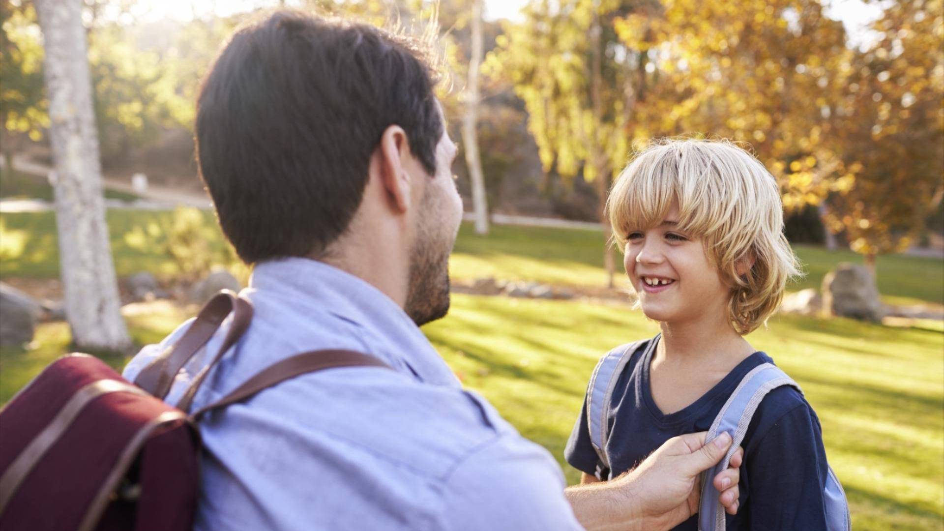Far og sønn som ser smilende på hverandre, begge med sekk på ryggen. 